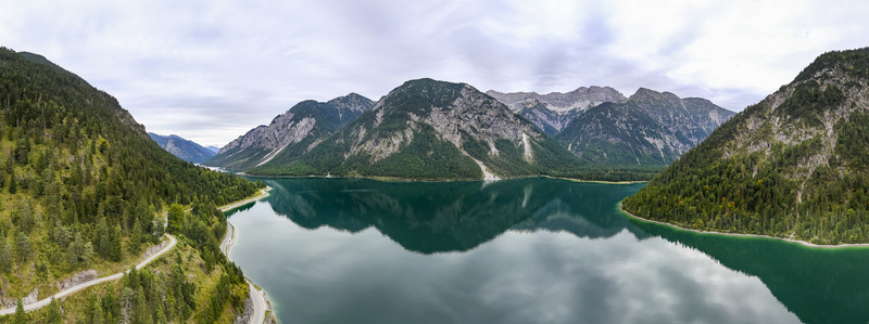Aerial view of Plansee s emerald waters mirror the dramatic forested mountains under a soft overcast sky Plansee Tyrol Austria. Aerial view of Plansee s emerald waters mirror the dramatic forested mountains under a soft overcast sky Plansee Tyrol Austria.
