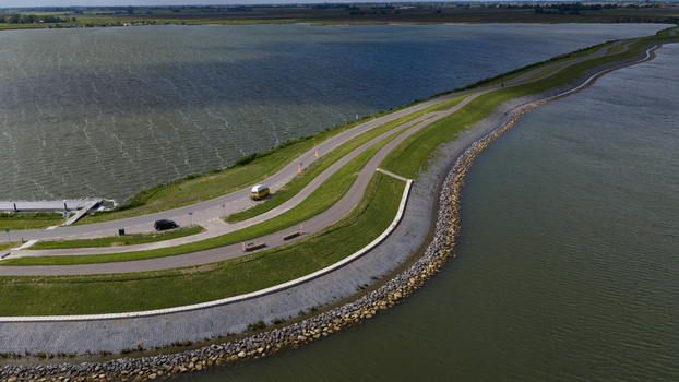 Aerial view of a winding dike road separating water bodies with a yellow van and a black car driving along the grassy embankment in Uitdam North Holland Netherlands.