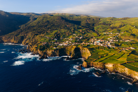Aerial view of the coastal village with green terraced fields and rugged cliffs overlooking the Atlantic Ocean in Ponta Delgada Acores Portugal. Aerial view of the coastal village with green terraced fields and rugged cliffs overlooking the Atlantic Ocean in Ponta Delgada Acores Portugal.