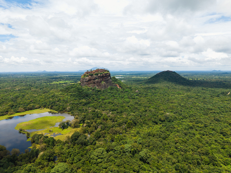 Aerial view of the ancient Sigiriya Lion Rock fortress rising above a vast green jungle landscape with a calm lake under a cloudy sky in Sigiriya Central Province Sri Lanka. Aerial view of the ancient Sigiriya Lion Rock fortress rising above a vast green jungle landscape with a calm lake under a cloudy sky in Sigiriya Central Province Sri Lanka.