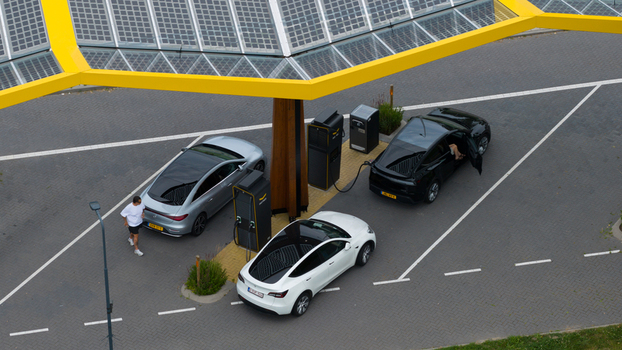 Krabbendijke Netherlands 28 June 2026 Aerial view of electric vehicles charging at a modern solar powered station with a yellow canopy featuring a man walking. Krabbendijke Netherlands 28 June 2026 Aerial view of electric vehicles charging at a modern solar powered station with a yellow canopy featuring a man walking.