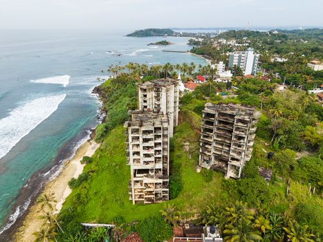 Aerial view of abandoned concrete buildings on a lush green cliff overlooking the turquoise ocean and coastline in Mirissa Southern Province Sri Lanka. Aerial view of abandoned concrete buildings on a lush green cliff overlooking the turquoise ocean and coastline in Mirissa Southern Province Sri Lanka.