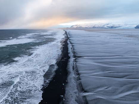 Aerial view of a snow covered black sand beach with crashing ocean waves under a dramatic cloudy sky in Iceland. Aerial view of a snow covered black sand beach with crashing ocean waves under a dramatic cloudy sky in Iceland.