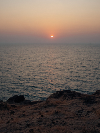 View of the sun dips low casting a warm glow over the tranquil sea as seen from the rugged cliffs Chiplun Maharashtra India. View of the sun dips low casting a warm glow over the tranquil sea as seen from the rugged cliffs Chiplun Maharashtra India.