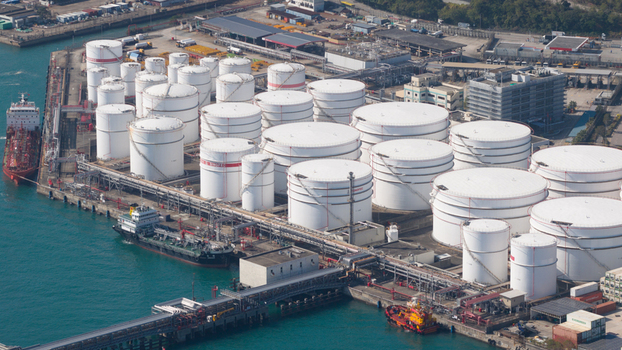 Aerial view of large white industrial oil storage tanks at a fuel terminal on the waterfront with cargo ships docked at the pier Hong Kong Hong Kong. Aerial view of large white industrial oil storage tanks at a fuel terminal on the waterfront with cargo ships docked at the pier Hong Kong Hong Kong.