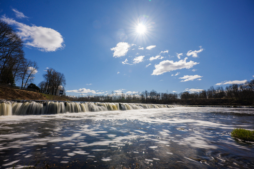 View of Ventas Rumba waterfall with flowing water under a bright sun and clear blue sky in Kuldiga Kuldigas novads Latvia. View of Ventas Rumba waterfall with flowing water under a bright sun and clear blue sky in Kuldiga Kuldigas novads Latvia.