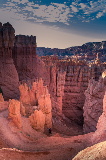 View of Bryce Canyon National Park with towering red rock hoodoos a winding trail and a hiker walking through the landscape under a blue sky in Utah United States.