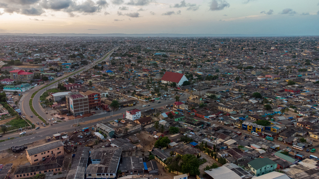 Aerial view of Teshie neighborhood featuring dense urban housing a prominent white building with a red roof and winding roads under a cloudy sky in Accra Greater Accra Region Ghana.
