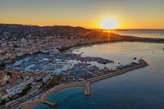 Aerial view of the harbor in Cannes at sunset featuring yachts and boats docked surrounded by coastal architecture and hills under a golden sky Cannes Provence Alpes Cote d Azur France. Aerial view of the harbor in Cannes at sunset featuring yachts and boats docked surrounded by coastal architecture and hills under a golden sky Cannes Provence Alpes Cote d Azur France.