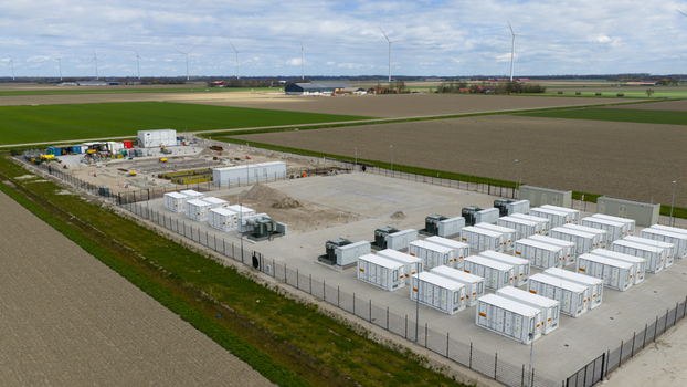 Aerial view of a battery energy storage system facility with rows of white containers and electrical equipment in a rural landscape with wind turbines in Dronten Flevoland Netherlands.