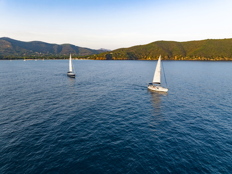Aerial view of sailboats sailing in the calm blue waters of Lacona Bay with green hills in the background in Lacona Tuscany Italy.