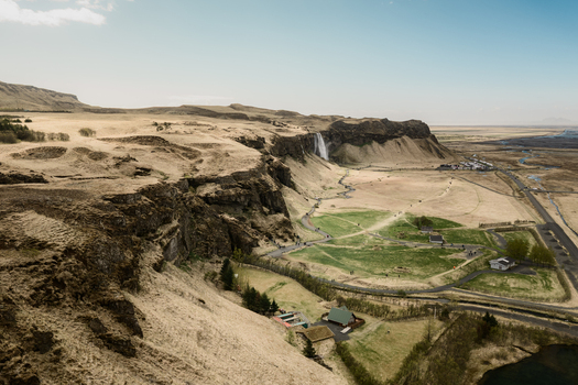 Aerial view of Seljalandsfoss waterfall cascading over rugged cliffs into a lush green valley with winding paths and surrounding volcanic landscape in Rangarthing eystra Iceland. Aerial view of Seljalandsfoss waterfall cascading over rugged cliffs into a lush green valley with winding paths and surrounding volcanic landscape in Rangarthing eystra Iceland.