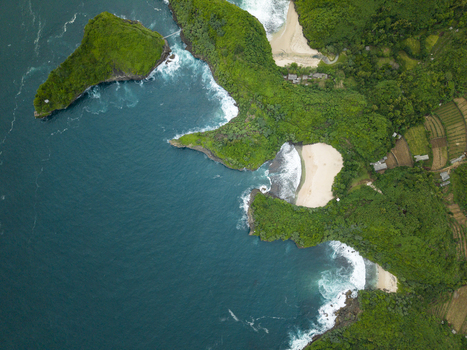 Aerial view of turquoise waters crashing against verdant cliffs and pristine white sands of Sedahan Beach Gunungkidul Regency Special Region of Yogyakarta Indonesia. Aerial view of turquoise waters crashing against verdant cliffs and pristine white sands of Sedahan Beach Gunungkidul Regency Special Region of Yogyakarta Indonesia.