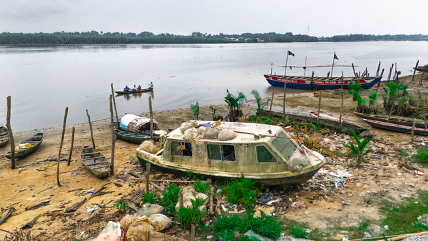 Aerial view of a riverbank featuring several small wooden boats a weathered cabin boat and people in a canoe on the water in Minima Rivers Nigeria.