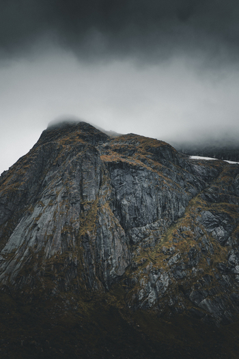 View of the Batman wall rock formation rising dramatically against a moody cloud covered sky in the rugged landscape of the Lofoten Islands Ramberg Nordland Norway. View of the Batman wall rock formation rising dramatically against a moody cloud covered sky in the rugged landscape of the Lofoten Islands Ramberg Nordland Norway.