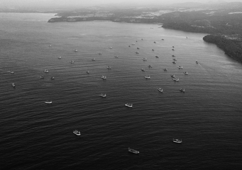 Aerial view of numerous fishing boats scattered across the sea near the misty coastline of Betul Beach in Mobor Beach Goa India.