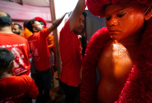 Munshiganj Bangladesh 13 April 2025 View of a young participant painted in striking orange and draped in a deep red garland stands solemnly amidst a crowd in crimson attire under warm light. Munshiganj Bangladesh 13 April 2025 View of a young participant painted in striking orange and draped in a deep red garland stands solemnly amidst a crowd in crimson attire under warm light.