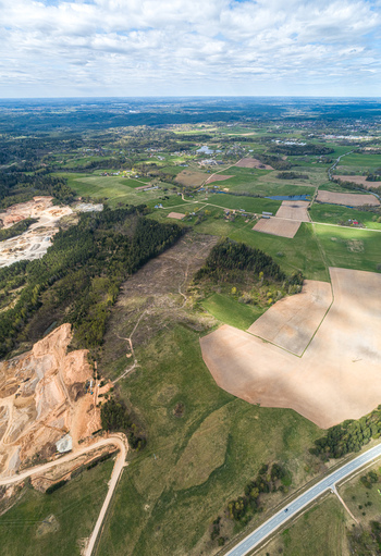 Aerial view of a rural landscape featuring a sand quarry agricultural fields patches of forest and a winding road under a cloudy sky in Latvia. Aerial view of a rural landscape featuring a sand quarry agricultural fields patches of forest and a winding road under a cloudy sky in Latvia.