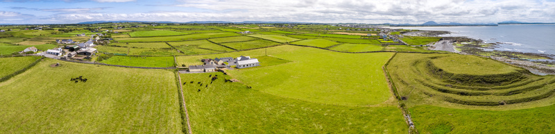 Aerial view of the historic ringfort site surrounded by lush green fields stone walls and grazing cattle along the rugged coastline in Enniscrone County Sligo Ireland. Aerial view of the historic ringfort site surrounded by lush green fields stone walls and grazing cattle along the rugged coastline in Enniscrone County Sligo Ireland.