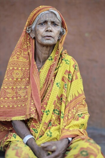 Odisha India 26 March 2026 View of an elderly woman with a weathered face adorned in a vibrant yellow and orange sari sitting solemnly against a textured earthen wall. Odisha India 26 March 2026 View of an elderly woman with a weathered face adorned in a vibrant yellow and orange sari sitting solemnly against a textured earthen wall.
