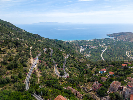 Aerial view of a winding mountain road through lush olive groves and historic stone houses overlooking the turquoise Ionian Sea in Qeparo Fshat Vlore County Albania. Aerial view of a winding mountain road through lush olive groves and historic stone houses overlooking the turquoise Ionian Sea in Qeparo Fshat Vlore County Albania.
