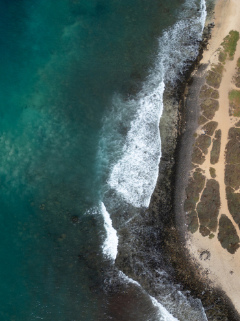 Aerial view of turquoise ocean waves crashing against a dark rocky shoreline and sandy paths Santa Maria Sal Cabo Verde. Aerial view of turquoise ocean waves crashing against a dark rocky shoreline and sandy paths Santa Maria Sal Cabo Verde.