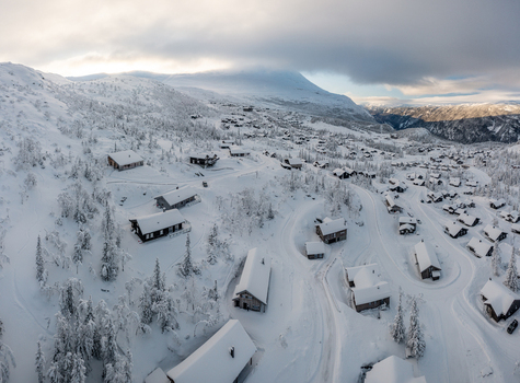 Aerial view of Gaustablikk Fjellresort with wooden cabins blanketed in deep snow surrounded by pine trees and rugged mountain peaks under a winter sky Rjukan Telemark Norway. Aerial view of Gaustablikk Fjellresort with wooden cabins blanketed in deep snow surrounded by pine trees and rugged mountain peaks under a winter sky Rjukan Telemark Norway.
