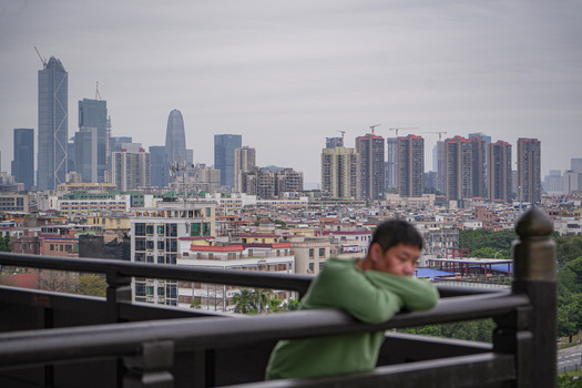 Guangzhou China 23 February 2024 View of a man leaning on a railing overlooking the modern skyline with high rise buildings and construction cranes under a cloudy sky. Guangzhou China 23 February 2024 View of a man leaning on a railing overlooking the modern skyline with high rise buildings and construction cranes under a cloudy sky.