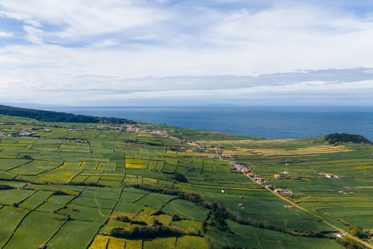 Aerial view of the lush green patchwork fields and coastal village of Terceira Island along the Atlantic Ocean under a cloudy sky Azores Portugal. Aerial view of the lush green patchwork fields and coastal village of Terceira Island along the Atlantic Ocean under a cloudy sky Azores Portugal.