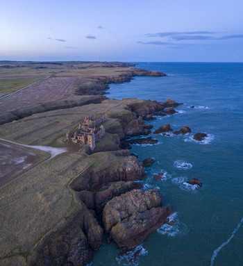 Aerial view of the ruins of Slains Castle perched on rugged cliffs overlooking the North Sea at twilight Cruden Bay Scotland United Kingdom. Aerial view of the ruins of Slains Castle perched on rugged cliffs overlooking the North Sea at twilight Cruden Bay Scotland United Kingdom.