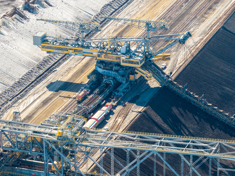 Aerial view of the Tagebau Welzow Sud brown coal open pit mine featuring a massive bucket wheel excavator operating along the dark earth terraces in Spremberg Brandenburg Germany. Aerial view of the Tagebau Welzow Sud brown coal open pit mine featuring a massive bucket wheel excavator operating along the dark earth terraces in Spremberg Brandenburg Germany.