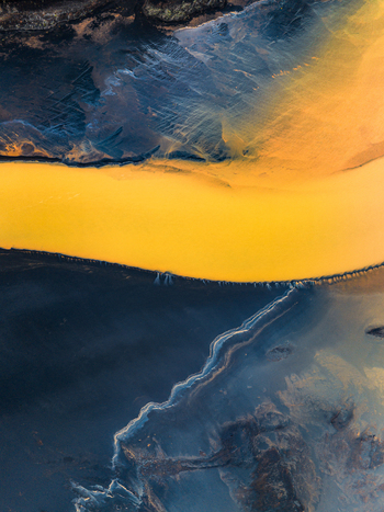 Aerial view of a vibrant yellow glacial river winding through dark volcanic sand deposits in Iceland. Aerial view of a vibrant yellow glacial river winding through dark volcanic sand deposits in Iceland.