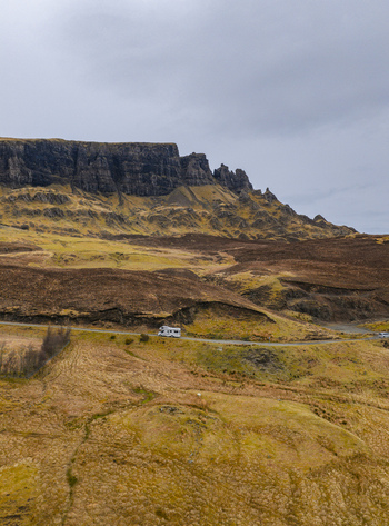 Aerial view of The Quiraing with a white campervan driving on a winding road through the rugged landscape under a cloudy sky Isle of Skye Scotland United Kingdom. Aerial view of The Quiraing with a white campervan driving on a winding road through the rugged landscape under a cloudy sky Isle of Skye Scotland United Kingdom.