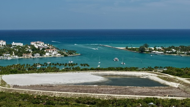 Aerial view of Peanut Island featuring turquoise waters boats navigating the inlet and white sand areas under a clear blue sky in Palm Beach County Florida United States.