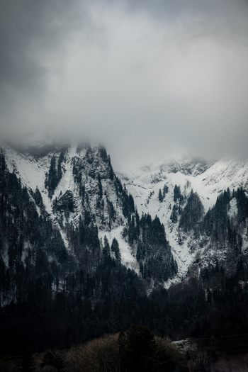 View of snow dusted peaks pierce the swirling clouds dark forests cling to the slopes creating a dramatic alpine vista Train from Lucerne to Interlaken Switzerland. View of snow dusted peaks pierce the swirling clouds dark forests cling to the slopes creating a dramatic alpine vista Train from Lucerne to Interlaken Switzerland.