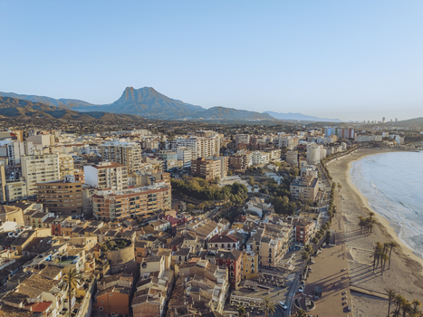 Aerial view of the coastal town featuring sandy beaches urban architecture and the majestic Puig Campana mountain under a clear blue sky in La Vila Joiosa Valencian Community Spain. Aerial view of the coastal town featuring sandy beaches urban architecture and the majestic Puig Campana mountain under a clear blue sky in La Vila Joiosa Valencian Community Spain.