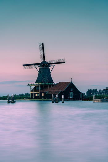 View of the historic Zaanse Schans Windmill standing by the calm water under a soft twilight sky with pink and blue hues Zaandam Noord Holland Netherlands. View of the historic Zaanse Schans Windmill standing by the calm water under a soft twilight sky with pink and blue hues Zaandam Noord Holland Netherlands.