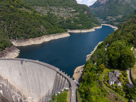 Aerial view of the Verzasca Dam and the deep blue waters of Lago di Vogorno surrounded by lush green mountains and stone houses in Gordola Ticino Switzerland. Aerial view of the Verzasca Dam and the deep blue waters of Lago di Vogorno surrounded by lush green mountains and stone houses in Gordola Ticino Switzerland.