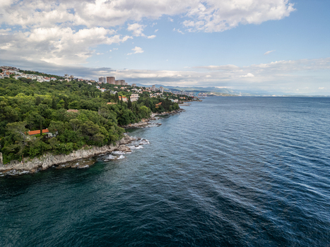 Aerial view of the coastline at Gradska plaza Razbojna with lush green vegetation rocky shores and the urban skyline of Rijeka in the distance Rijeka Croatia. Aerial view of the coastline at Gradska plaza Razbojna with lush green vegetation rocky shores and the urban skyline of Rijeka in the distance Rijeka Croatia.