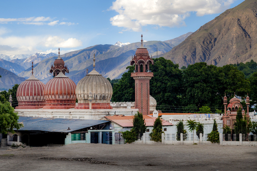 View of the historic Shahi Mosque with its distinctive red and white domes and tall minaret set against the backdrop of the Hindu Kush mountains in Chitral Khyber Pakhtunkhwa Pakistan.