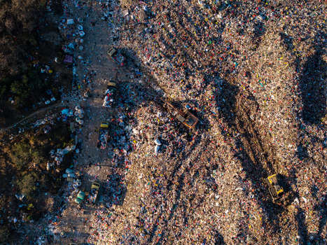 Aerial view of TPA Suwung landfill with heavy machinery and trucks working on large piles of waste in Kecamatan Denpasar Selatan Bali Indonesia.