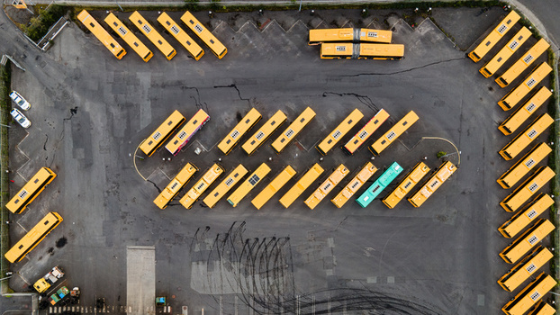 Aerial view of a bus depot with rows of yellow buses and one teal bus parked on an asphalt lot in Reykjavik Reykjavikurborg Iceland.