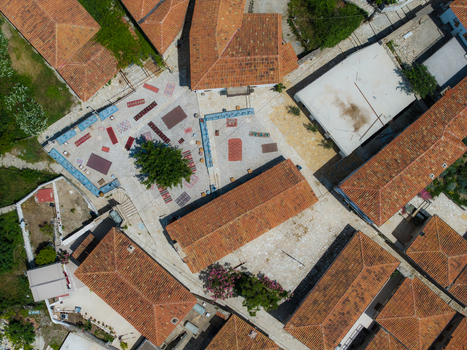 Aerial view of traditional red tiled rooftops surrounding a stone courtyard with a central tree and decorative rugs in Dhermi Vlore County Albania. Aerial view of traditional red tiled rooftops surrounding a stone courtyard with a central tree and decorative rugs in Dhermi Vlore County Albania.