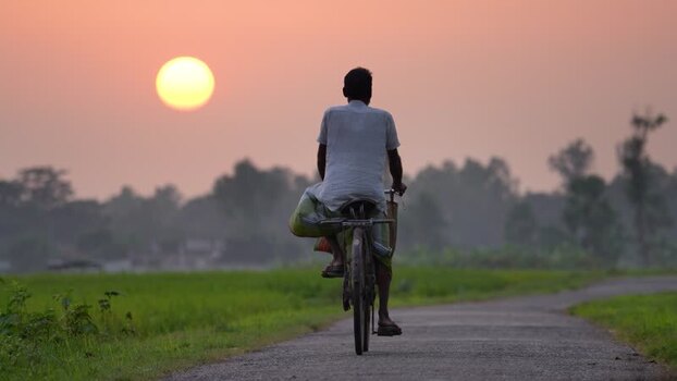 View of a man riding a bicycle on a rural road at sunset Bangladesh. View of a man riding a bicycle on a rural road at sunset Bangladesh.