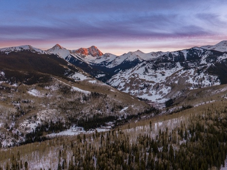Aerial view of Capitol Peak at winter sunset with snow covered slopes dense pine forests and the rugged terrain of the Rocky Mountains in Aspen Colorado United States.