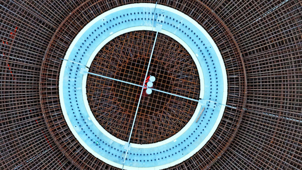 Aerial view of a circular wind turbine foundation featuring intricate steel rebar reinforcement and a central concrete ring in Latvija. Aerial view of a circular wind turbine foundation featuring intricate steel rebar reinforcement and a central concrete ring in Latvija.