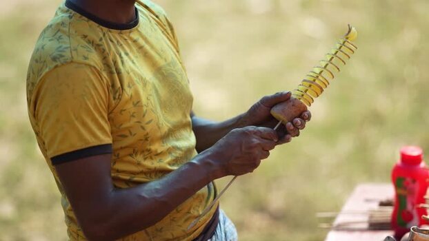 View of a man preparing a spiral potato on a skewer Bangladesh. View of a man preparing a spiral potato on a skewer Bangladesh.