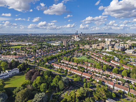 Aerial view of residential neighborhoods with rows of houses green parks and a distant urban skyline under a blue sky with scattered clouds in Brentford England United Kingdom. Aerial view of residential neighborhoods with rows of houses green parks and a distant urban skyline under a blue sky with scattered clouds in Brentford England United Kingdom.