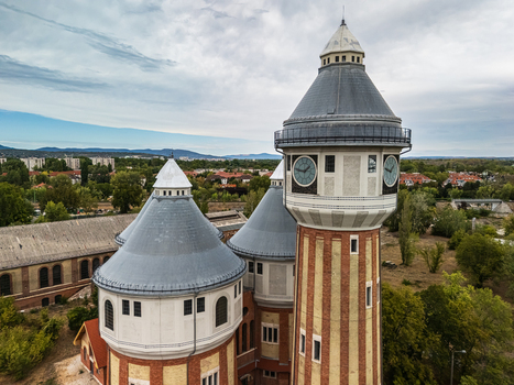 Aerial view of the restored historic towers of the former Obuda Gasworks above industrial buildings trees and residential neighborhoods in Budapest Hungary. Aerial view of the restored historic towers of the former Obuda Gasworks above industrial buildings trees and residential neighborhoods in Budapest Hungary.