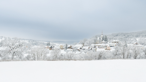 View of a snow covered village with houses trees and a church spire under a cloudy winter sky in Alba Iulia Alba County Romania. View of a snow covered village with houses trees and a church spire under a cloudy winter sky in Alba Iulia Alba County Romania.